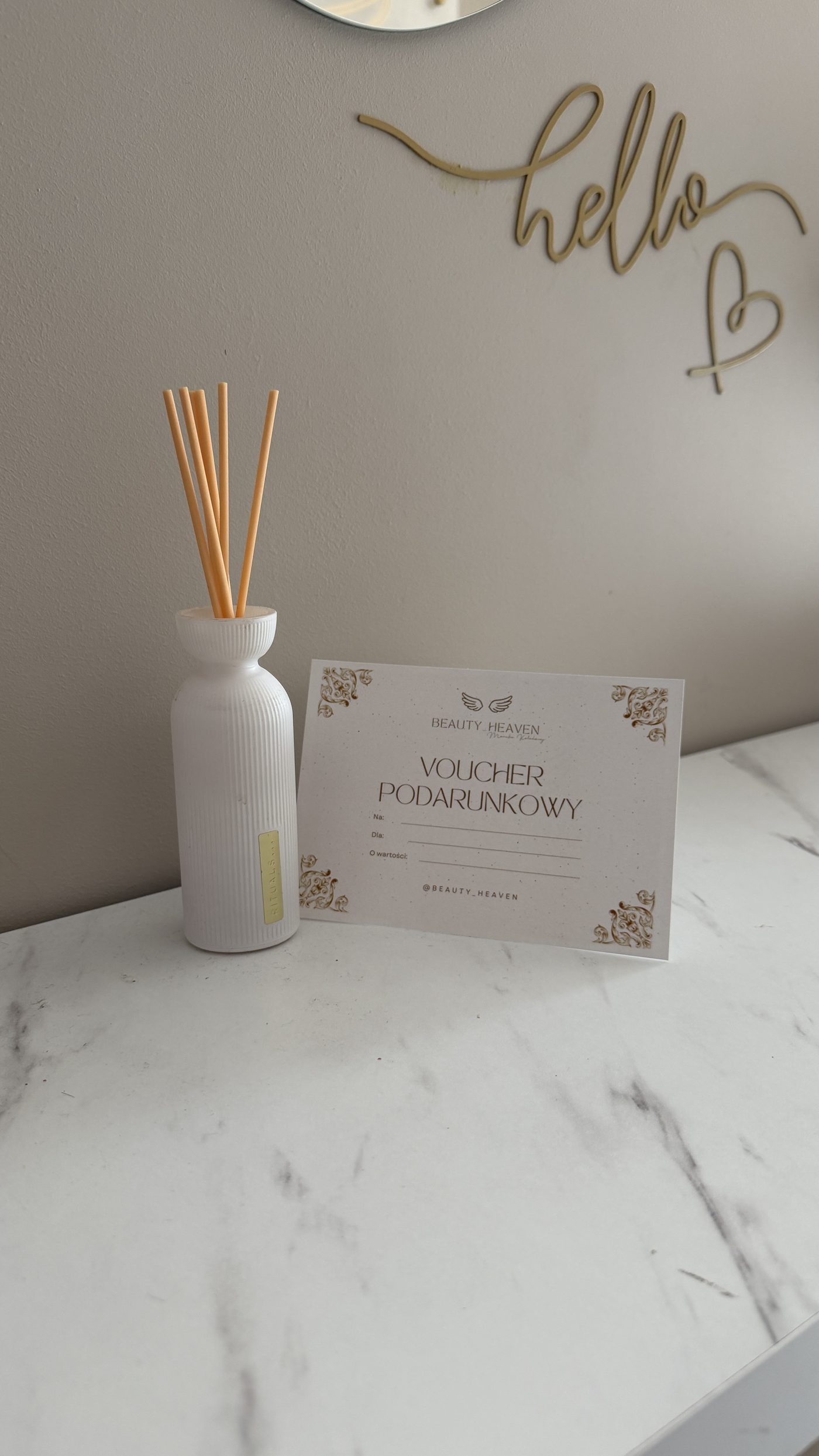 Voucher podarunkowy Beauty Heaven ustawiony obok białego dyfuzora zapachowego na marmurowym blacie